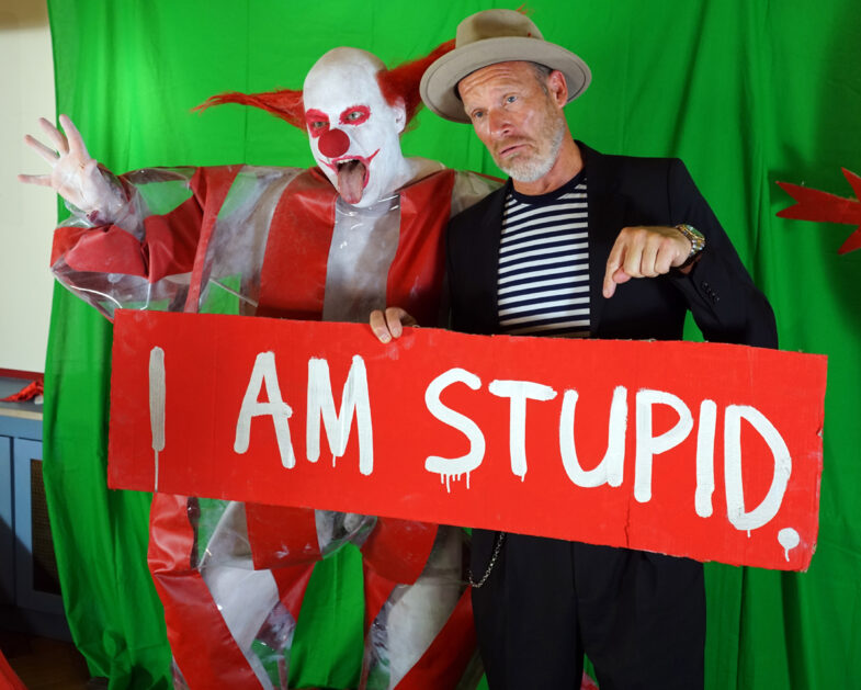 horror clown Schluba, A the man René Holm, with a shield on which the taboo is written: i am stupid.
