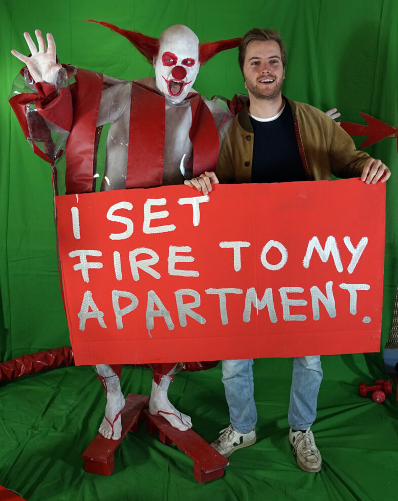 horror clown Schluba, A man with a shield on which the taboo is written:  I Sset fire to my apartment.
