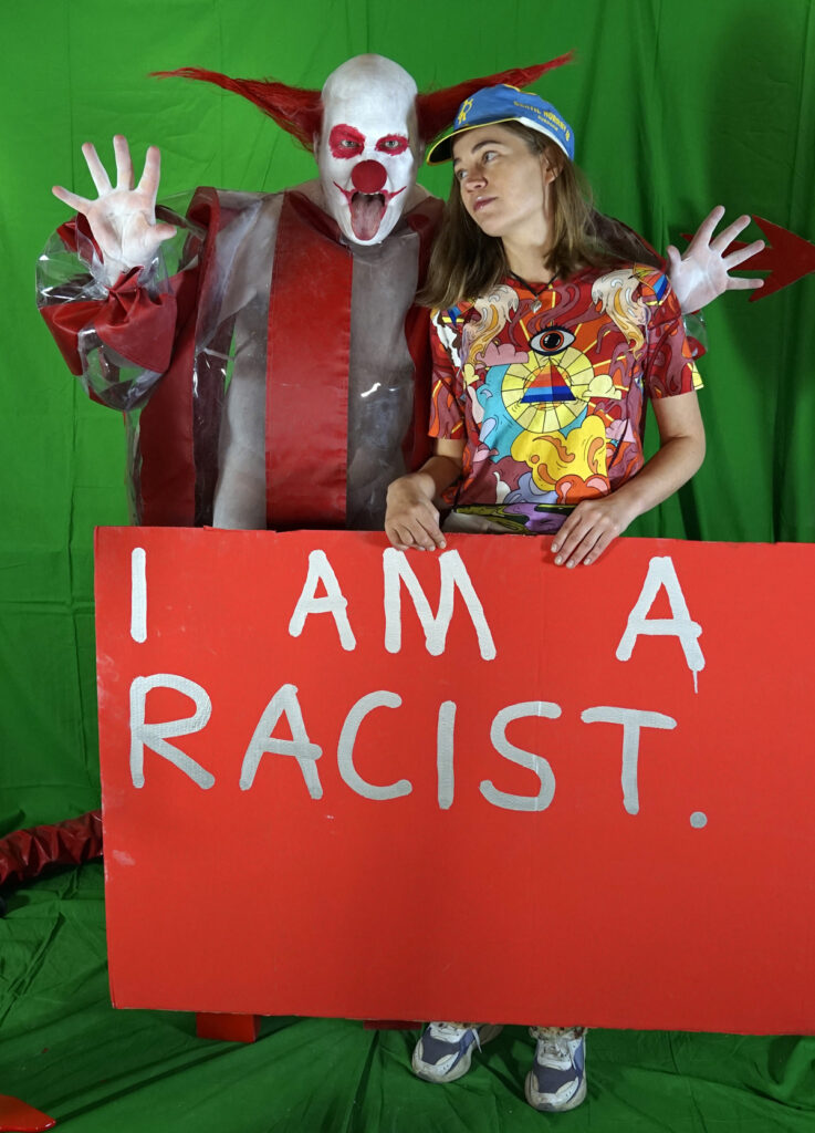 horror clown Schluba, A woman with a shield on which the taboo is written: I am a Racist.