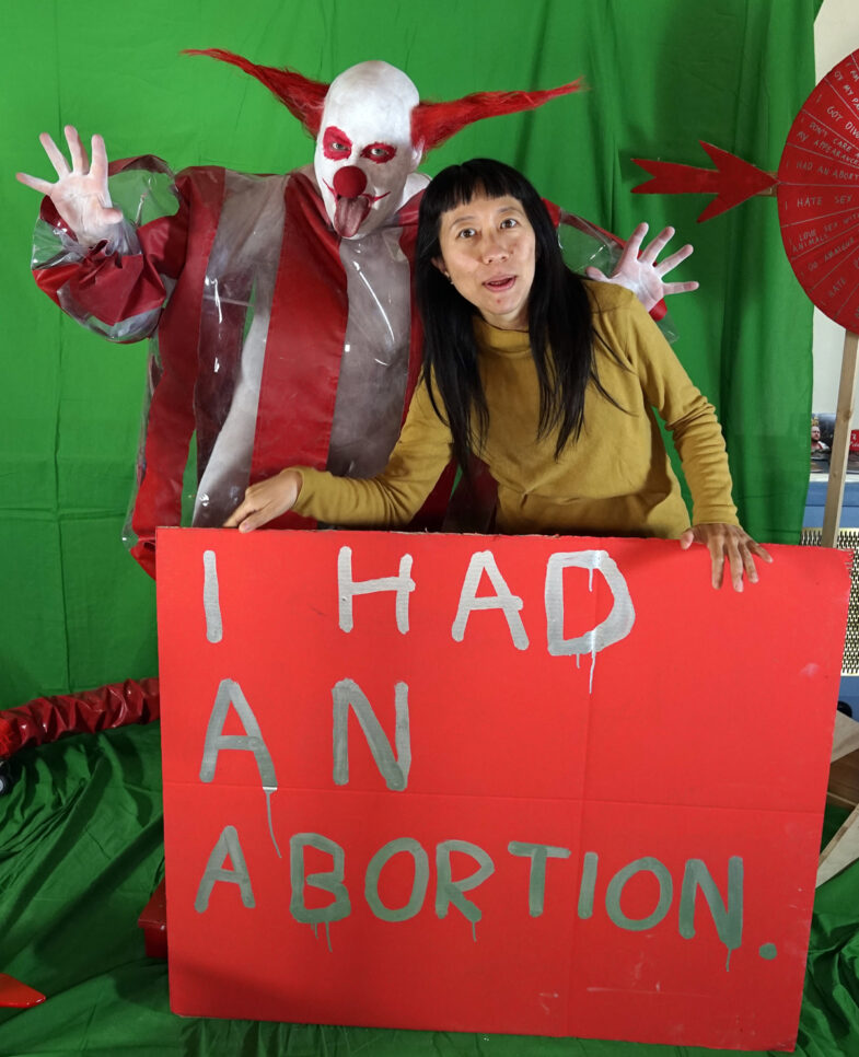 horror clown Schluba, A woman with a shield on which the taboo is written: I had an abortion.